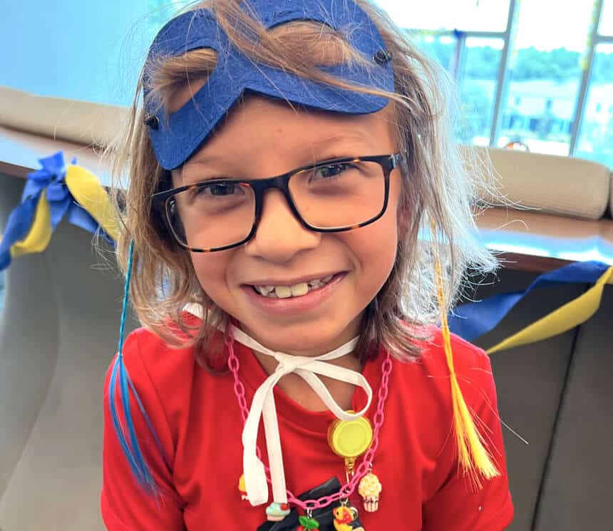 A child with glasses smiling and wearing a costume inside.