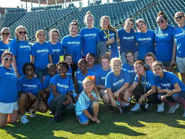 A group of volunteers posing on a baseball field weraing Dreams Come True Volunteer shirts.